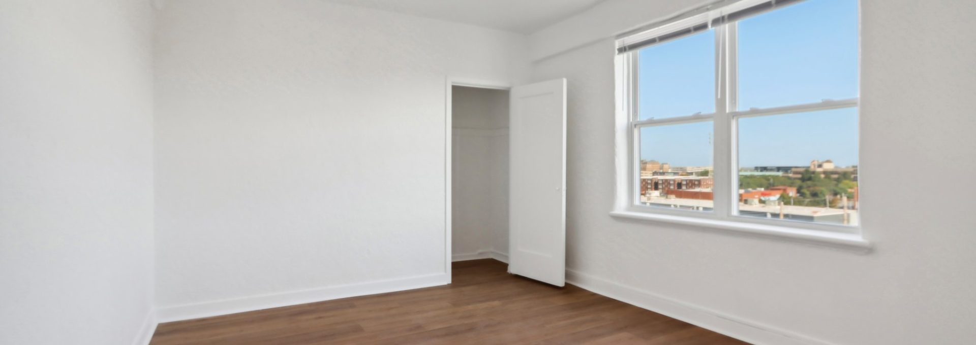 an empty room with hardwood floors and a window at The St Regis Apartments