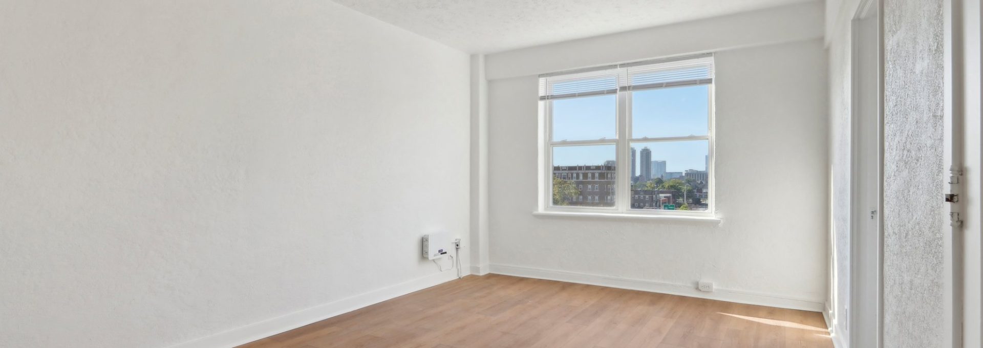 an empty room with hardwood floors and a window at The St Regis Apartments